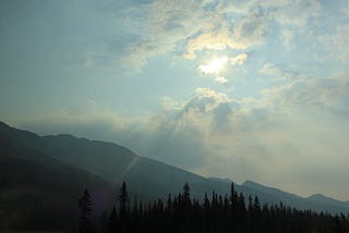 The sun glowing behind the clouds in a mountain scene.