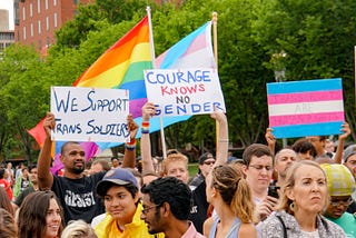 3 protest signs read: We support trans soldiers. Courage knows no gender. Trans rights are human rights.