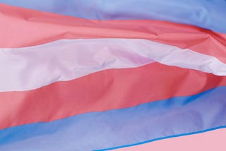 Image of the transgender flag with blue, pink and white horizontal stripes waving.