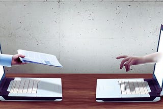 Dwie osoby przekazujące sobie dokument przez ekrany laptopów — symboliczne przedstawienie tematu jak napisać podanie o pracę i przesłać je online.