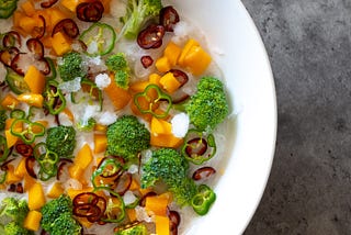 Broccoli, carrots and peppers in a bowl filled with ice.