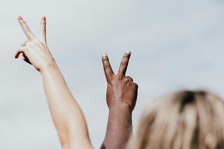 Two people holding up the Peace sign, one person has pale skin the other has dark Black skin