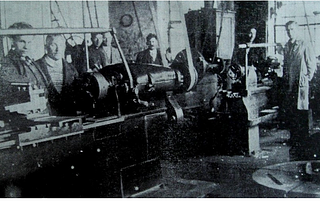 My father Wolf Zylbersztajn and my grandfather inside the Hasag factory standing behind a factory work table.