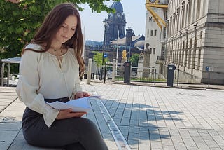 Woman sitting down and reading against a picturesque city background.