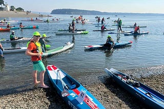 Ivan standing on shore at the start of the race next to paddleboards, surfskis, and outrigger canoes