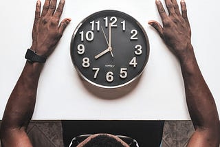Um homem negro de óculos em frente a um relógio.