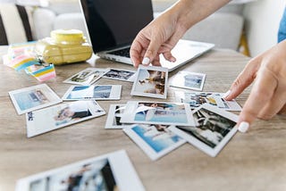 Pictures scattered on a table with a camera and a laptop.