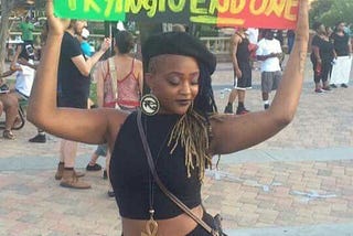 A Black person holding a colourful sign saying“We’re not trying to start a race war we’re trying to end one”