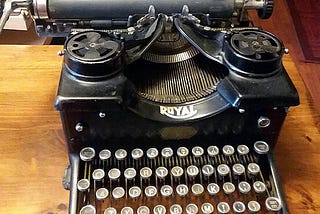 A 1909 Royal antique typewriter with a blank sheet of paper sits on a wooden desk.