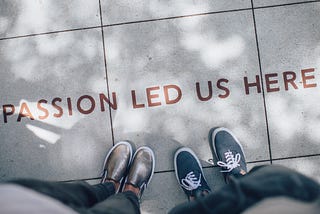 two sets of feet on a sidewalk in front of a phrase that says “passion led us here”