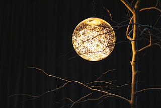 A globe light hung to look like the moon, illuminating a bare tree.