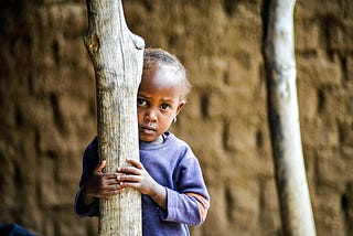 Image of a small black girl holding unto a tree as she looks on in fear. This depicts how I looked growing up in my environment.