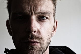 A young white man has half his face in shadow as he looks worried