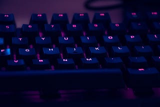 A keyboard bathed in purple light with glowing letters in pink on keys.