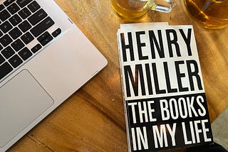 Cafe table photo of laptop, tea, and the book “The Books in My Life” by Henry Miller.
