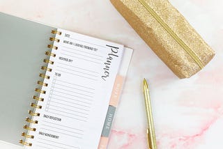 Ein typisches Influencer-Bild, bei dem alles gestellt ist: Ein Planer, ein goldener Kuli, eine goldene Tasche. Photo by Emma