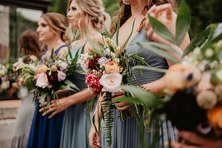 4 people stand wearing complementary green dresses and holding pink bouquets