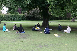 A circle of seven people sit in meditation in Regents Park, London.