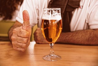 Close up of an Aussie glass of a beer with a man’s hand giving a thumbs up.