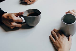 Two sets of hands holding coffee cups implying a man and woman in conversation