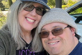 Woman (author) and her adult son with Down syndrome wearing hats and smiling at the camera.