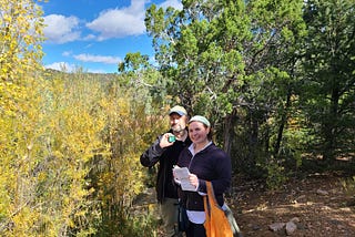 Dr. Henry “Trae” Winter and MaryKay Severino smiling outdoors with a notebook and an AudioMoth recorder.