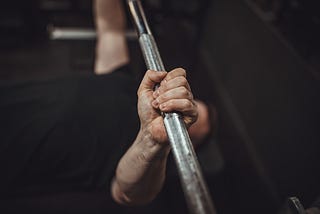 A pair of hands grip a barbell, pushing upward.