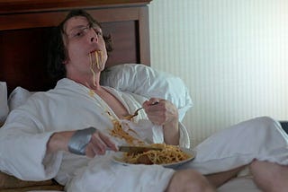 A man lays in bed and eats spaghetti.