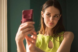Young woman with brown hair holding a phone and taking a selfie
