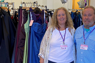 Heidi and John pictured in front of a rack of prom dresses