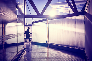 Image: the silhouette of a woman with a big handbag passing between opaque sheets of glass on a pedestrian bridge in Oslo