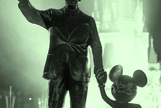 Walt Disney and Mickey Mouse statues in silhouette against Magic Kingdom in background.