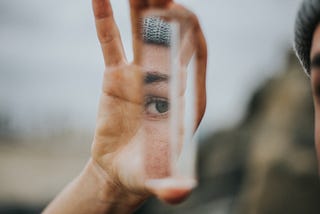 Hand holding a piece of glass reflecting an eye and eyebrow.