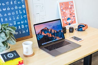 Macbook on a desk with some wireframes and posters.