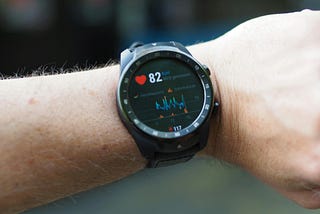 A Fitbit watch worn on a man’s wrist showing heart rate in bpm.