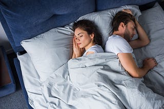 A man and woman sleep peacefully back to back in bed.