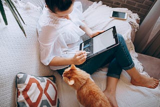 Woman on the sofa with an orange tabby cat and her tablet computer