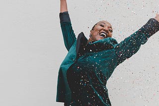 A woman smiling and standing with her hands in the air, throwing confetti.