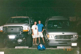 Two guys in between a lifted Ford Excursion SUV and our road trip van, Modesto, California, July 3, 2001