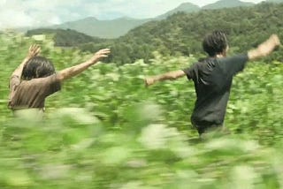 Mugino Minato dan Hoshikawa Yori berlarian bersama di padang rumput dalam cuplikan adegan film Monster (2023)