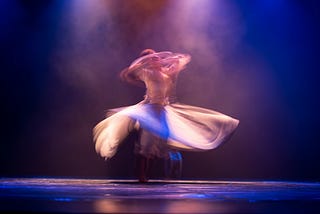 Dancer spinning on stage, blurred under purple stage lights, symbolizing the process of transformation and expansion