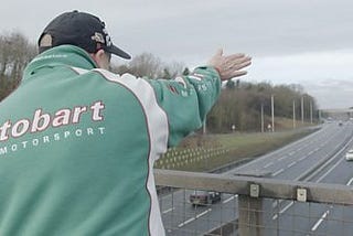 Barry May, the ‘Waving Man’, is pictured giving his ‘last wave’ to lorries on the A19 motorway. He is a white man wearing a baseball cap and a Motorsport sweatshirt.