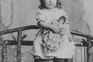A black and white photo of a chubby cheeked Victorian child clutching a doll