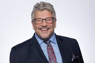 Profile picture of Wynn Hausser, a smiling middle-aged White man with glasses and a goatee.