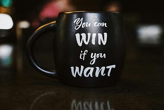 Close up photo of black mug that says “you can win if you want” in white font