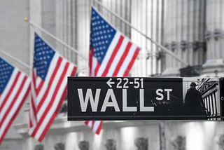 The Wall Street street sign with American flags in the background.