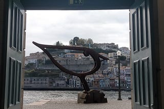 Huge bird sculpture overlooking a river, seen through an open door