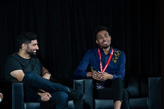 Nima Ghamsari, a Persian man in a black t-shirt, and Ulyssses Smith, a Black man in a blue collared shirt, on stage