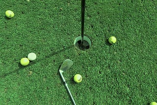 Golf balls scattered around the hole, with a club laying next to them.