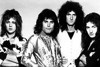 Roger Taylor, Freddie Mercury, Brian May, and John Deacon of the band Queen photographed in 1975, wearing glam outfits and teased hairdos, looking directly at the camera